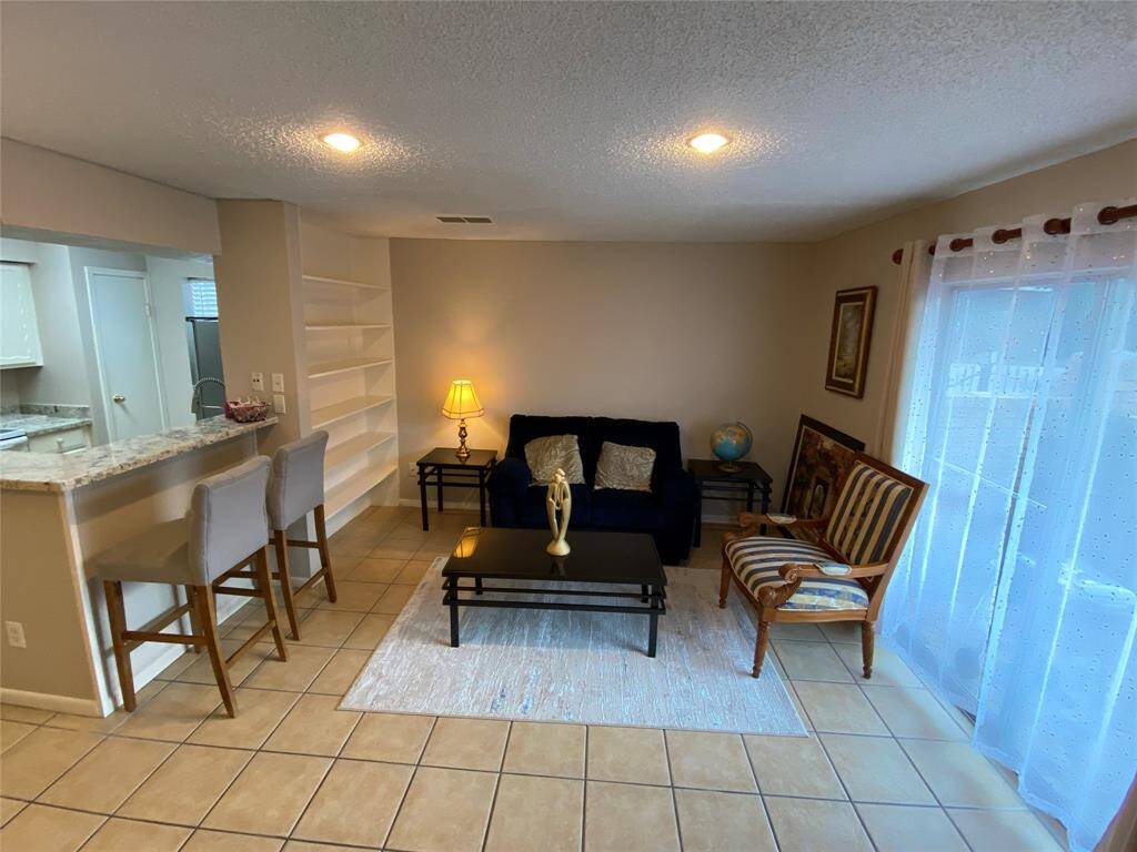 This living area features tile flooring, seating arrangement, and a breakfast bar and ample natural light from the sliding glass door, creating a warm and inviting atmosphere.