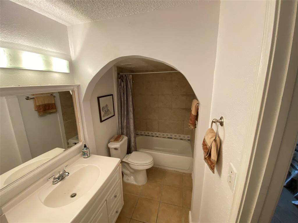 It includes a tiled bathtub and shower area with a decorative archway. The neutral tiles and walls create a bright, welcoming space.