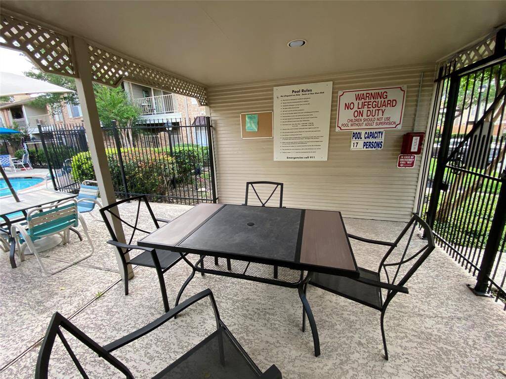 This photo shows a covered outdoor seating area next to a pool, featuring a table and chairs. It's part of a communal space with safety signage and a view of the pool and surrounding greenery, ideal for relaxation and social gatherings.