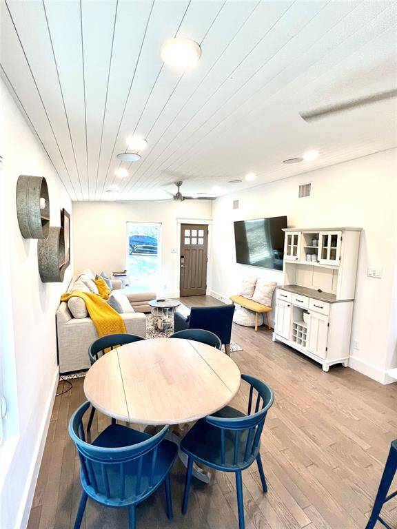 Bright and modern open-concept living area with a cozy sectional sofa, stylish decor, and a well-equipped kitchen. The space features wood flooring, recessed lighting, and large sliding doors leading to an outdoor area, creating a seamless indoor-outdoor flow.
