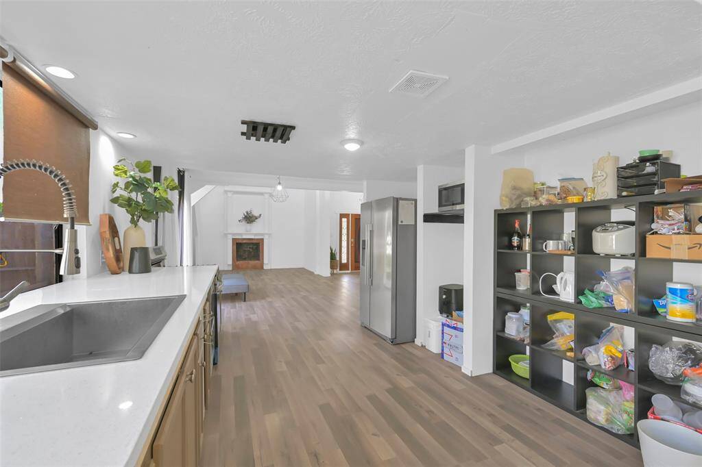 This spacious open-concept kitchen and living area features LVP floors, a modern sink, a large refrigerator, and ample storage. A cozy fireplace enhances the living space, creating a warm atmosphere ideal for family gatherings.