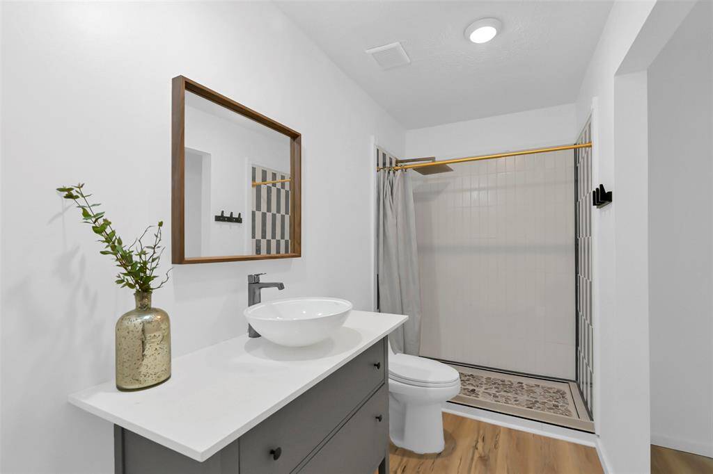 This bathroom features a modern design with a sleek vanity and vessel sink.  It includes a spacious shower with tile accents offering a clean and bright atmosphere.