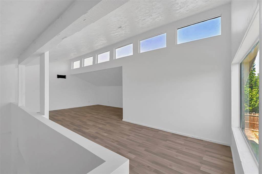 This bright, open loft features high ceilings, modern LVP flooring, and abundant natural light through upper and side windows, creating a spacious and inviting atmosphere.