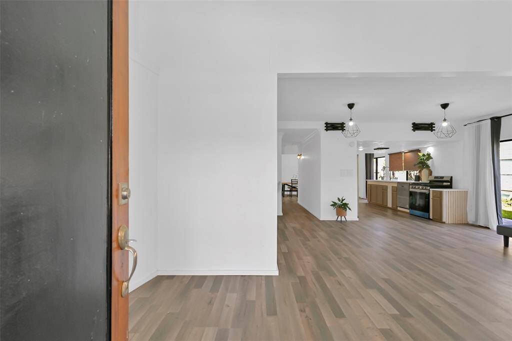 This photo showcases a bright, open-concept entryway leading into a spacious kitchen and living area. It features light flooring, modern lighting fixtures, and ample natural light from large windows.