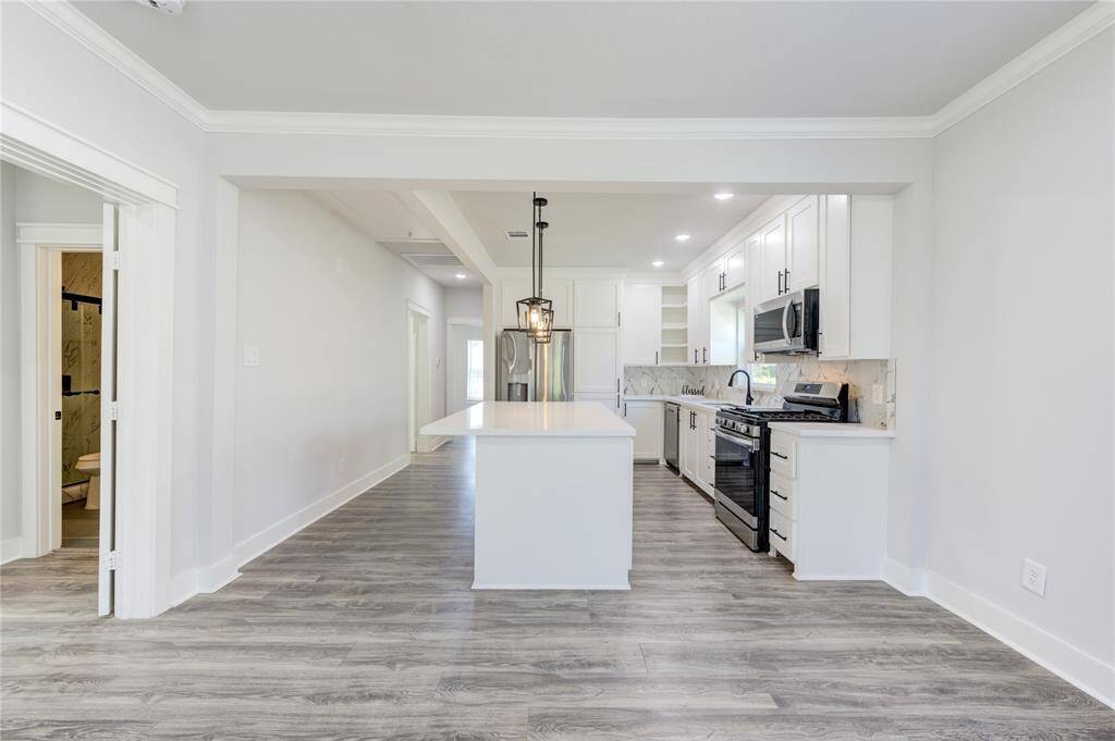 This photo showcases a modern, open-concept kitchen with sleek white cabinets, stainless steel appliances, and a central island. The space features light wood flooring and ample natural light, creating a bright and inviting atmosphere.