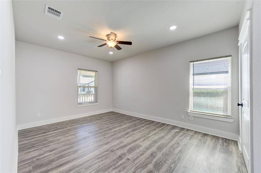 This room features modern wood-look flooring, neutral walls, and ample natural light from two windows. It includes recessed lighting, a ceiling fan, and a closet, making it versatile for various uses.