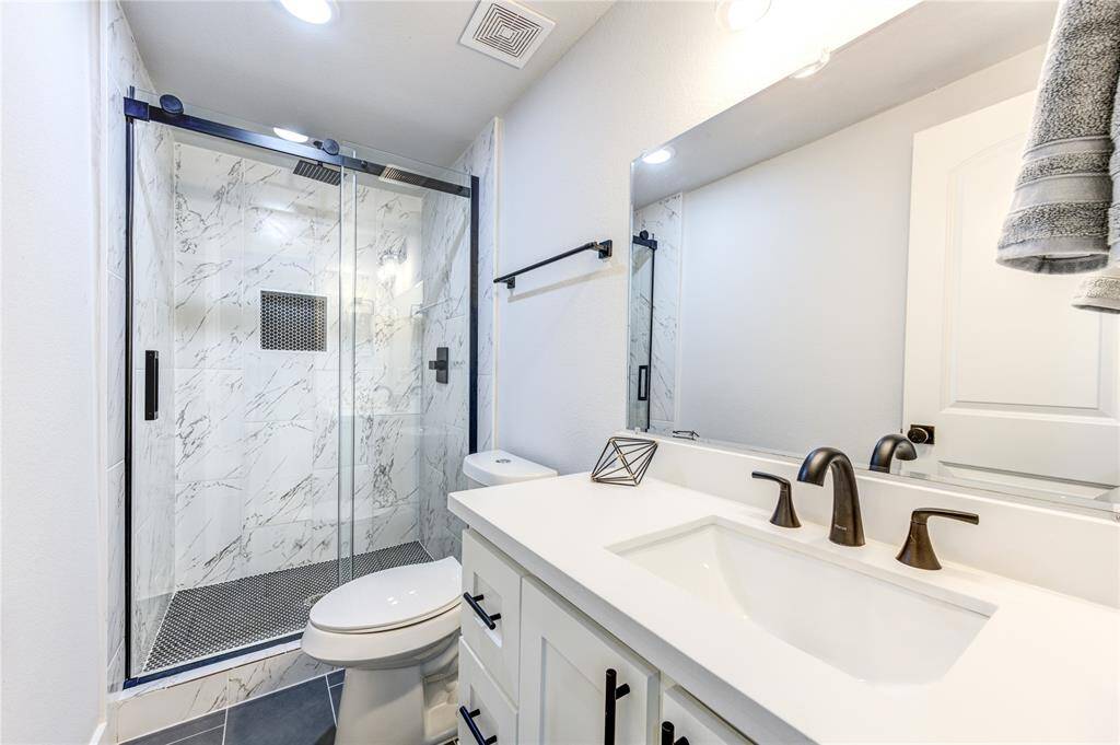 Modern bathroom with a sleek design featuring a glass-enclosed shower with marble-style tiles, a white vanity with dual sinks, and stylish matte black fixtures.