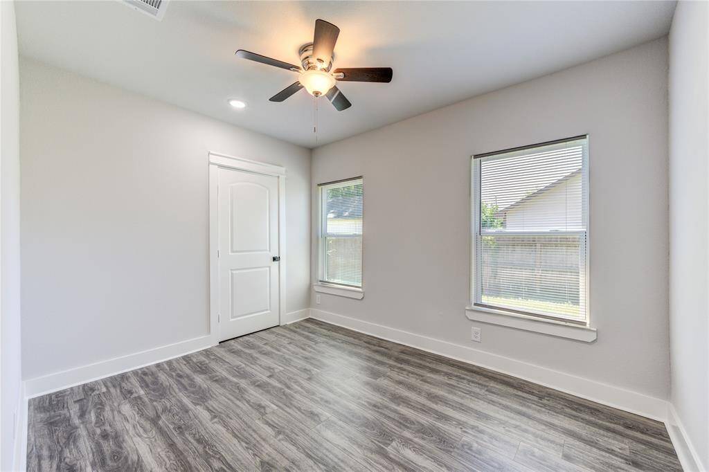 Bright and airy bedroom featuring sleek flooring, ample natural light from dual windows, and a modern ceiling fan.