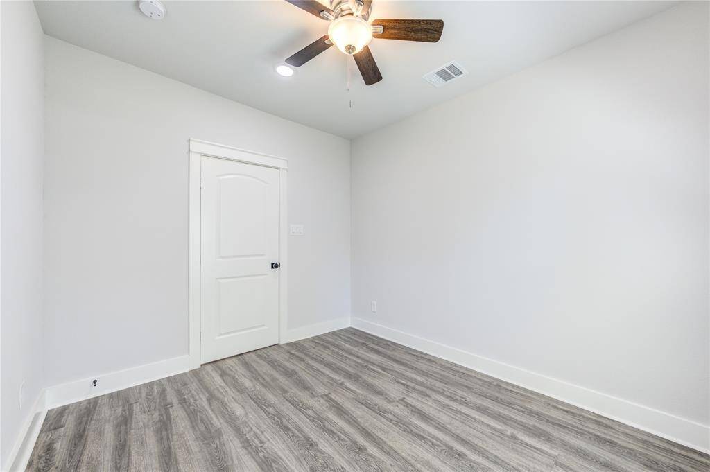 This room features light gray walls, wood-style flooring, and a ceiling fan with a light fixture, creating a bright and modern space.
