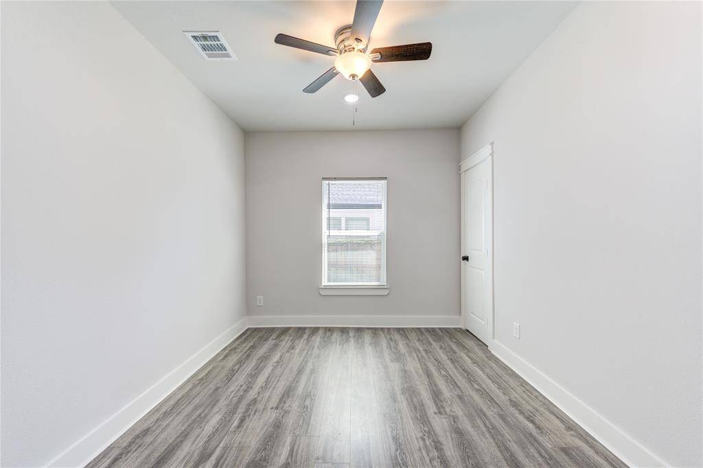 This room features a modern look with light gray walls and wood-look flooring. It includes a ceiling fan and a window that provides natural light, making it bright and inviting.