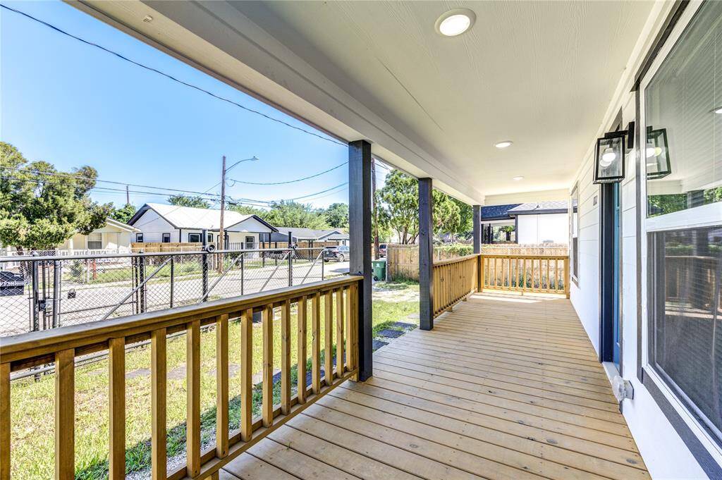 This photo showcases a spacious, covered front porch with wooden decking and railings, offering a welcoming entry to the home. The porch provides a pleasant view of the neighborhood, featuring nearby houses and greenery, ideal for relaxation.