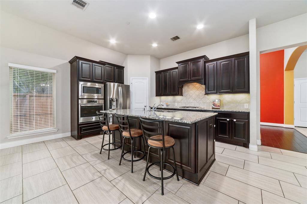Stunning kitchen featuring rich dark wood cabinetry, granite countertops, built-in storage within the island, stainless steel appliances, and a spacious pantry for all your essentials