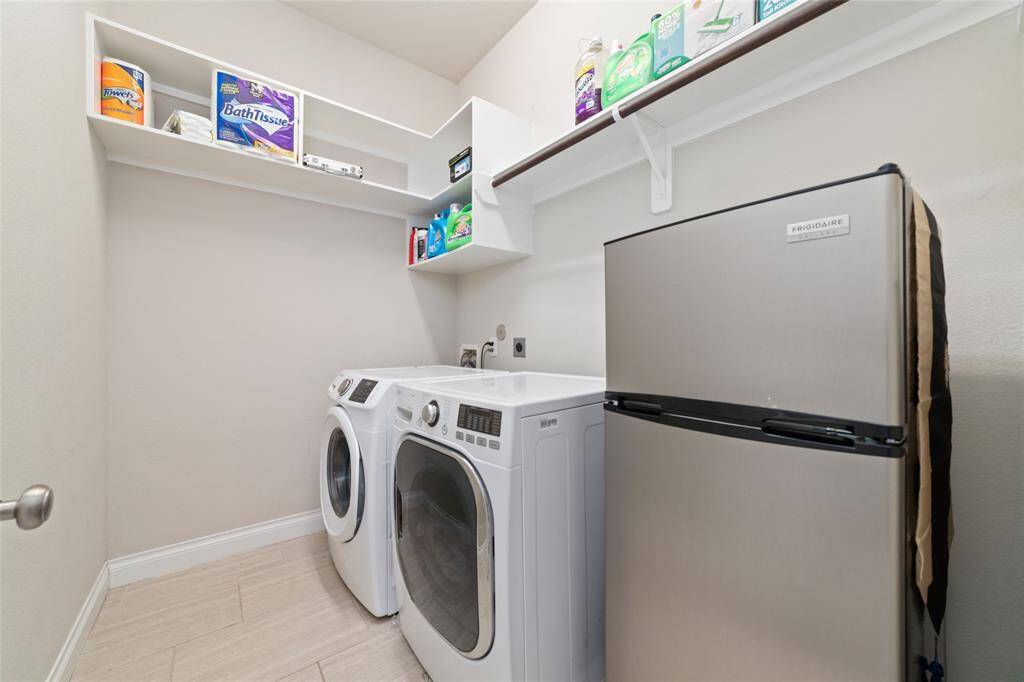 Spacious utility room featuring built-in storage shelves and ample space for an additional refrigerator. NOTE: Washer, Dryer, and Refrigerator are excluded from the sale of the home