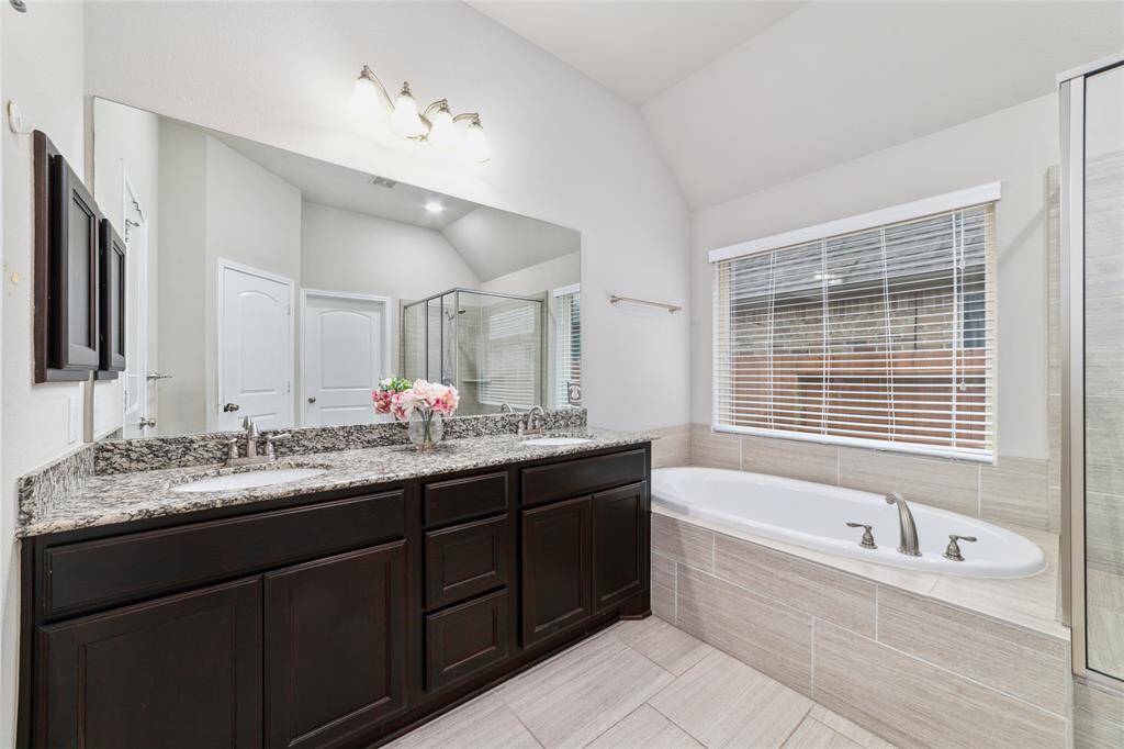 Spacious primary bathroom suite featuring double sinks with granite countertops, an elongated soaking tub, and abundant natural light