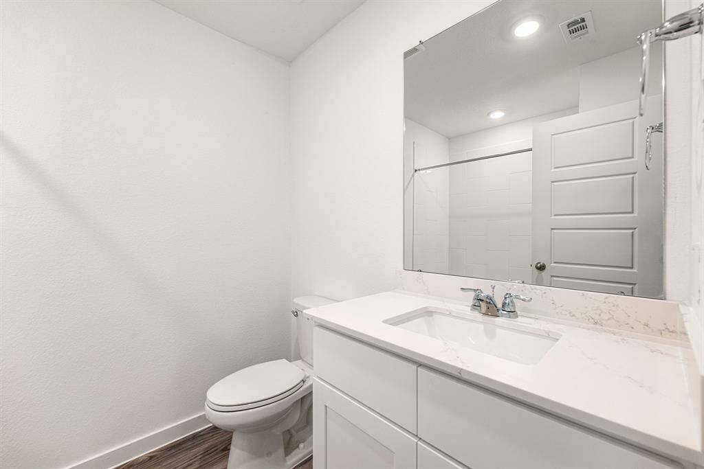 This modern secondary bath features sleek finishes, a bright white vanity with a marble-look countertop, and a large mirror that enhances the sense of space. Recessed lighting and contemporary fixtures complete the clean, polished look.
