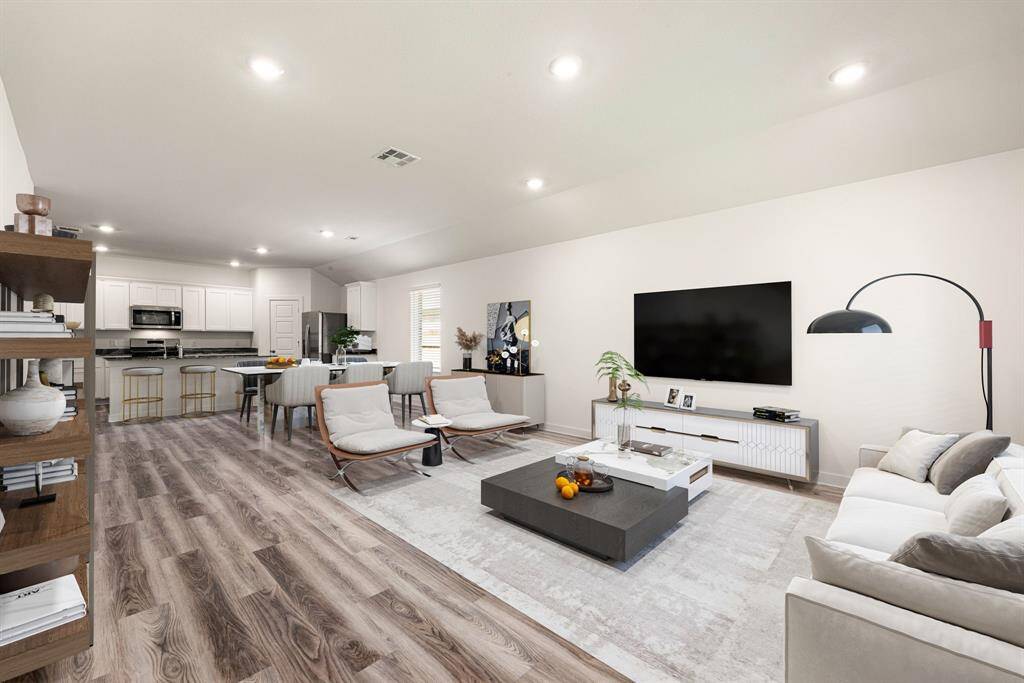This open-concept living space showcases beautiful wood-look vinyl plank flooring, recessed lighting, and a seamless flow into the kitchen and dining areas. With neutral tones, high ceilings, and abundant natural light, it offers a warm and spacious atmosphere perfect for everyday living and entertaining.