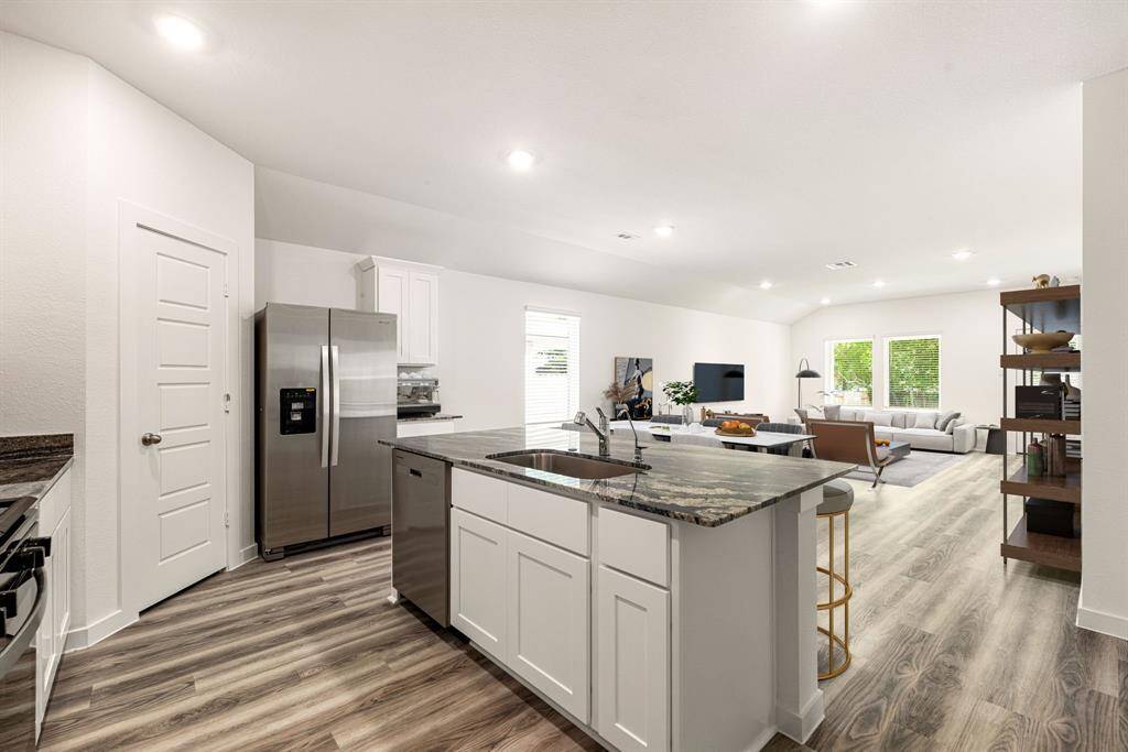 Step into this stunning open-concept kitchen and living space featuring sleek granite countertops, stainless steel appliances, and modern white cabinetry. The spacious island with an undermount sink offers ample prep space, while the wide plank flooring adds a touch of contemporary elegance. Abundant natural light and recessed ceiling lights create a bright, inviting atmosphere perfect for entertaining or relaxing.