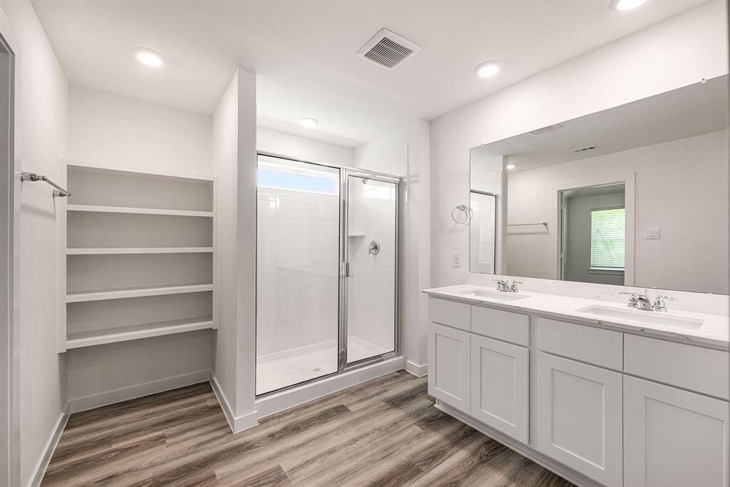 Enjoy a spa-like experience in the expansive walk-in shower with elegant tile surround, while bright cabinetry and light countertops create a fresh, airy ambiance. Thoughtful built-in shelving offers stylish storage, complemented by soaring ceilings and sleek, dark modern finishes that add a sophisticated touch. A perfect blend of luxury and functionality awaits.