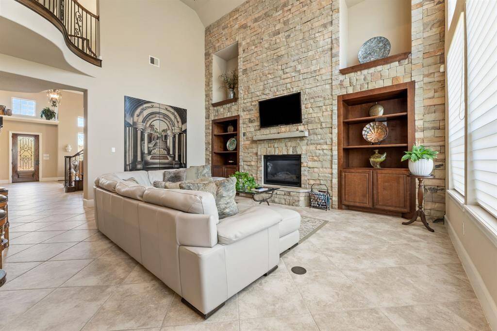The centerpiece of this grand living area is the floor-to-ceiling stone fireplace, flanked by custom-built shelves and accent niches that add depth and character.