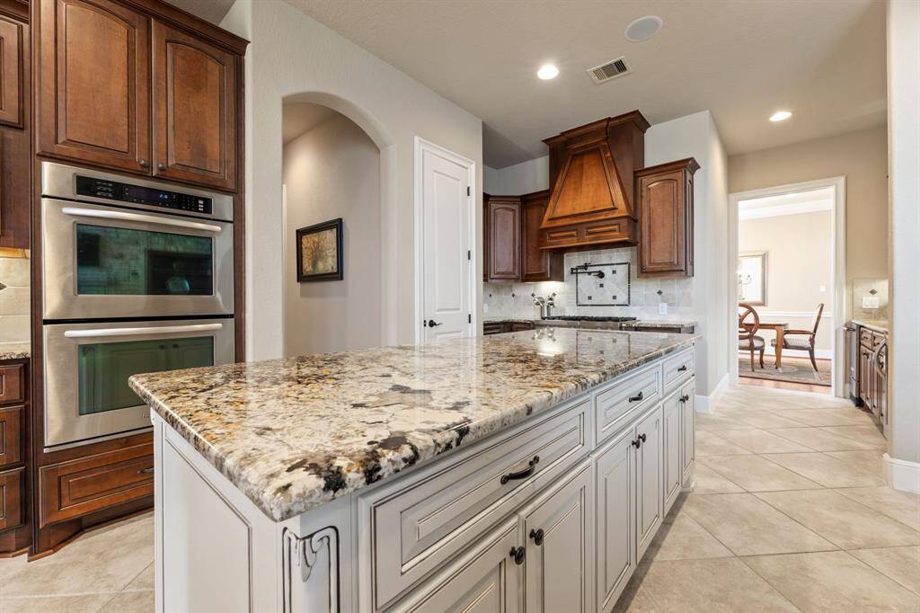 A striking central island with a gleaming granite countertop anchors the kitchen, while an open doorway leads to the formal dining room beyond.