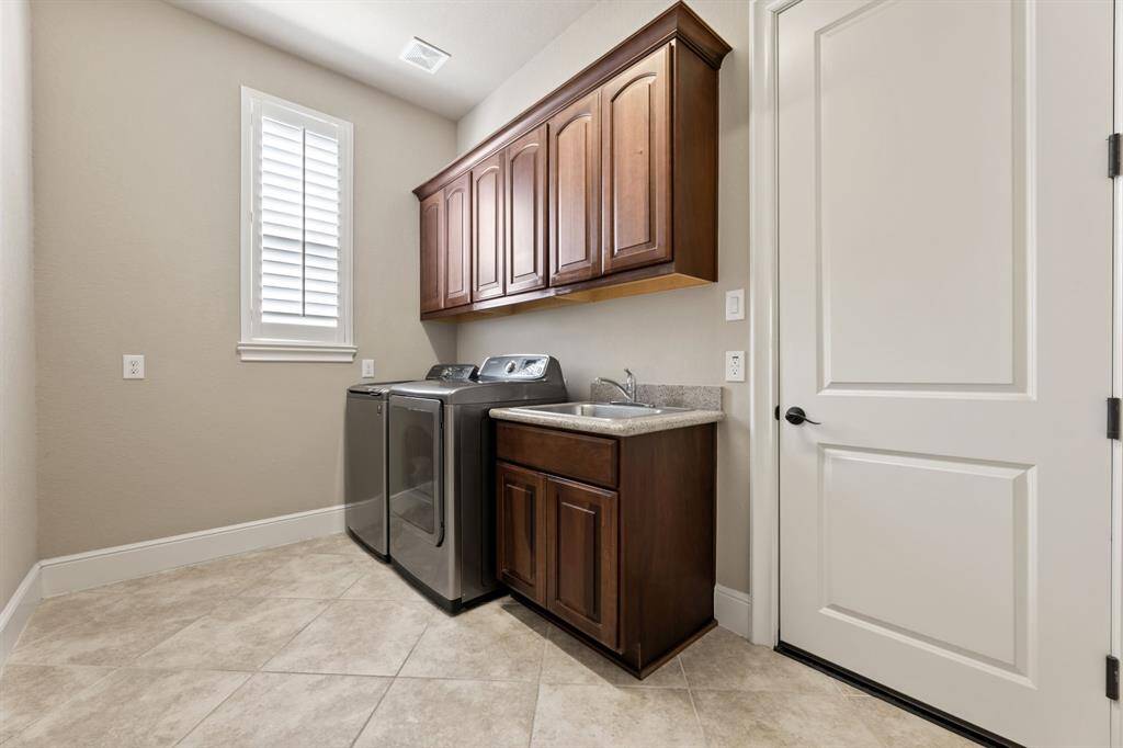 The laundry room has dark wood cabinets overhead, plus a sink with under storage, ensuring functionality meets style.