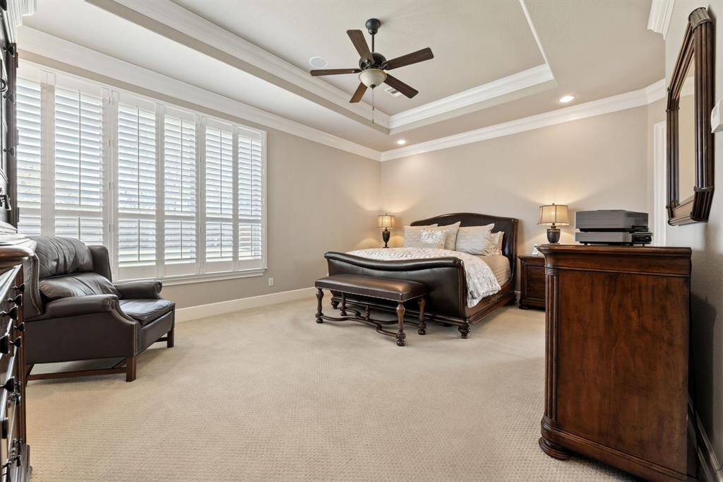 The primary bedroom is an expansive, carpeted sanctuary with room for a cozy sitting area, a tray ceiling, and large windows that bathe the space in daylight.