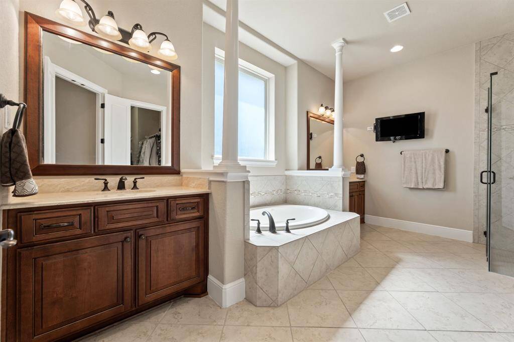 Twin vanities with framed mirrors flank a regal soaking tub, set beneath a window that welcomes soft, natural light.