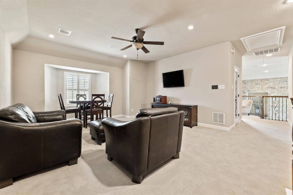 This game room is a versatile upstairs retreat with space for multiple seating arrangements, complemented by a ceiling fan and recessed wall with a window.