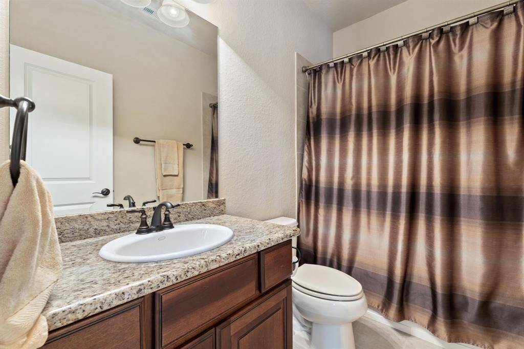 This bathroom shows a continuation of the home’s elegant aesthetic, featuring a wooden vanity with storage and a large mirror.