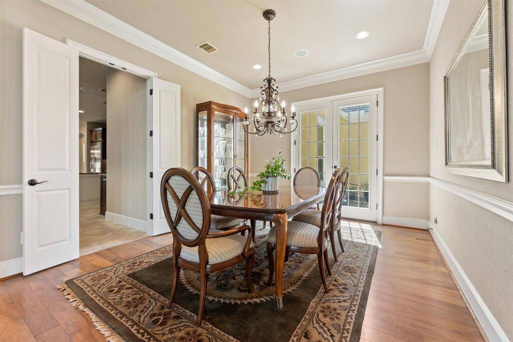 A timeless dining space featuring rich walnut hardwood floors, French doors, and a striking chandelier that adds a touch of elegance.