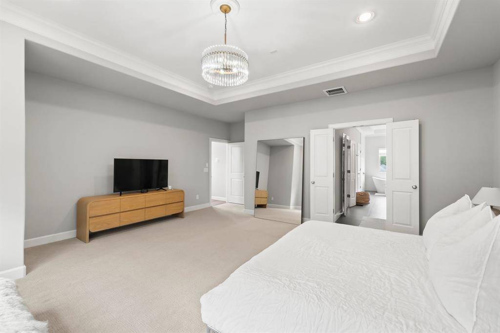 Spacious primary bedroom featuring elegant tray ceilings, custom lighting, and ample space for a cozy sitting area.