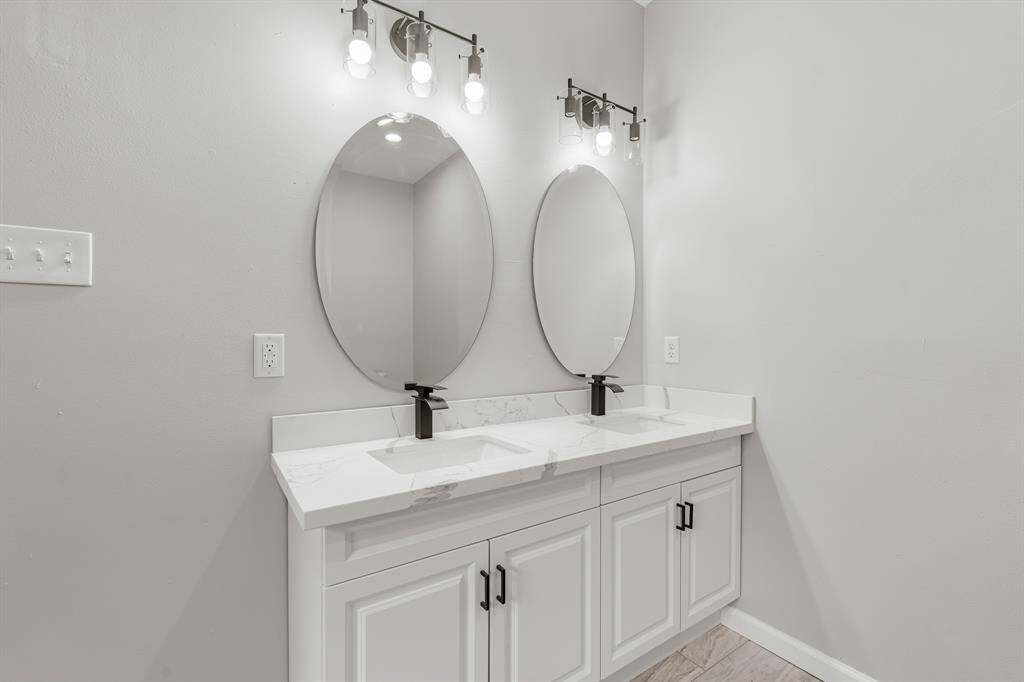 Primary Bathroom, featuring double sinks, two round mirrors, quartz countertops with white cabinets, and stunning vanity lights.