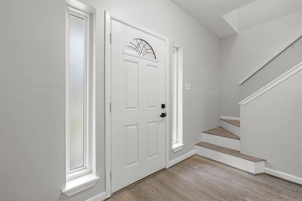 Stunning front foyer, featuring vinyl plank floors, elegant wood staircases and a stunning white door.