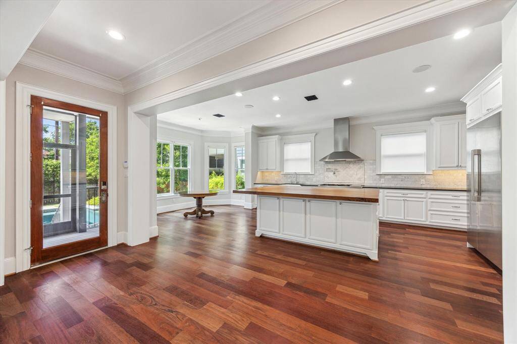 Bright and Inviting Culinary Space: This expansive kitchen and dining area is flooded with natural light through floor-to-ceiling windows and elegant French doors. The open layout boasts gleaming hardwood floors, a spacious central island, and crisp white cabinetry, creating a perfect setting for both casual meals and entertaining.