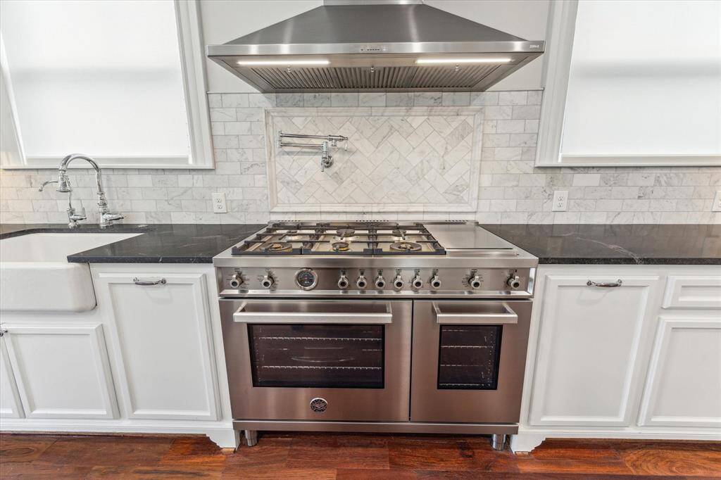 Professional-Grade Culinary Center: This stunning kitchen features a premium stainless steel gas range with double ovens, crowned by a sleek, high-performance vent hood. A marble backsplash and convenient pot filler complete this chef’s paradise, blending style with functionality.