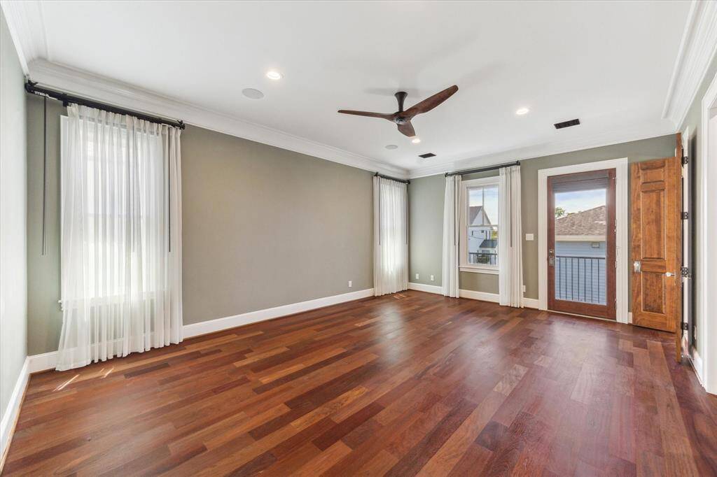 Expansive Primary Retreat: This generously sized primary bedroom offers rich hardwood floors, serene natural light, and direct access to a private balcony. Enhanced by soft drapery and a sleek ceiling fan, it is a perfect sanctuary for rest and relaxation.
