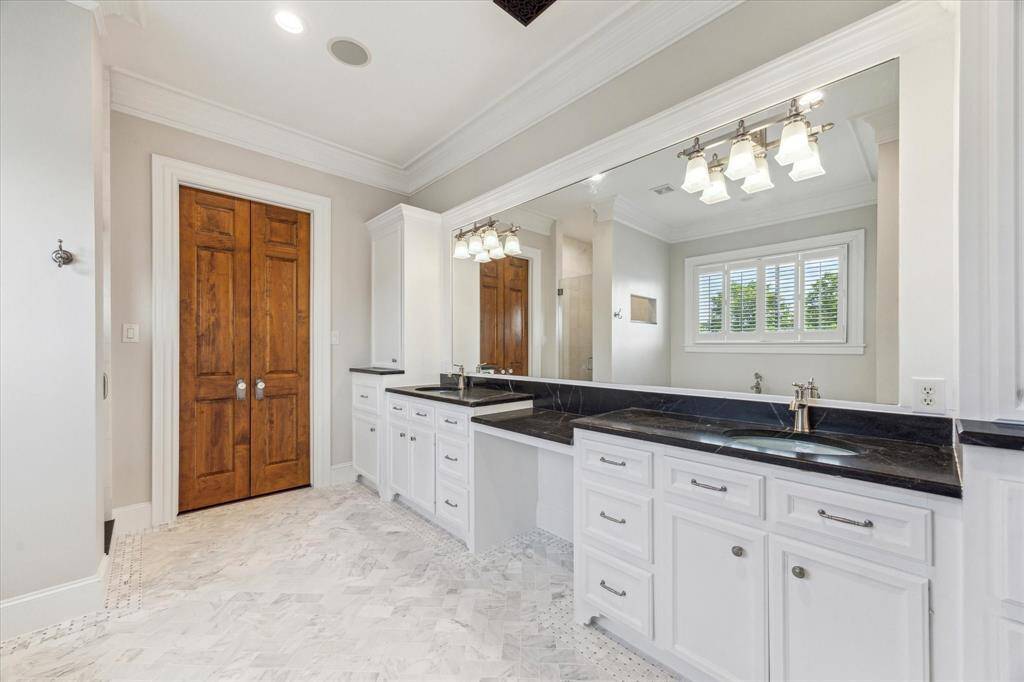 Luxurious Primary Bathroom: A spa-like sanctuary featuring dual vanities with sleek black countertops, elegant white cabinetry, and a beautifully tiled floor. The expansive mirror and warm lighting create a bright, refreshing atmosphere for your daily routine.