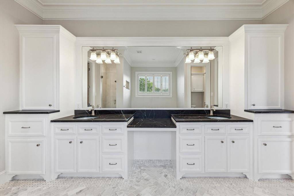 Grand Dual Vanity Oasis: This expansive primary bathroom offers a stunning double vanity setup with sleek black countertops, pristine white cabinetry, and a massive mirror that amplifies light and space. The elegant lighting fixtures and marble-inspired flooring add a touch of luxury to this serene retreat.