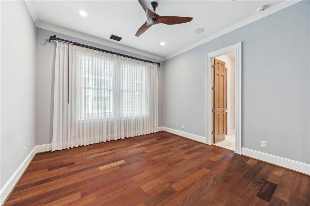 Bright and Spacious Second Bedroom: This inviting secondary bedroom offers warm hardwood floors, a sleek ceiling fan, and ample natural light through elegant sheer drapery. A tranquil and versatile space for guests, family, or a home office.