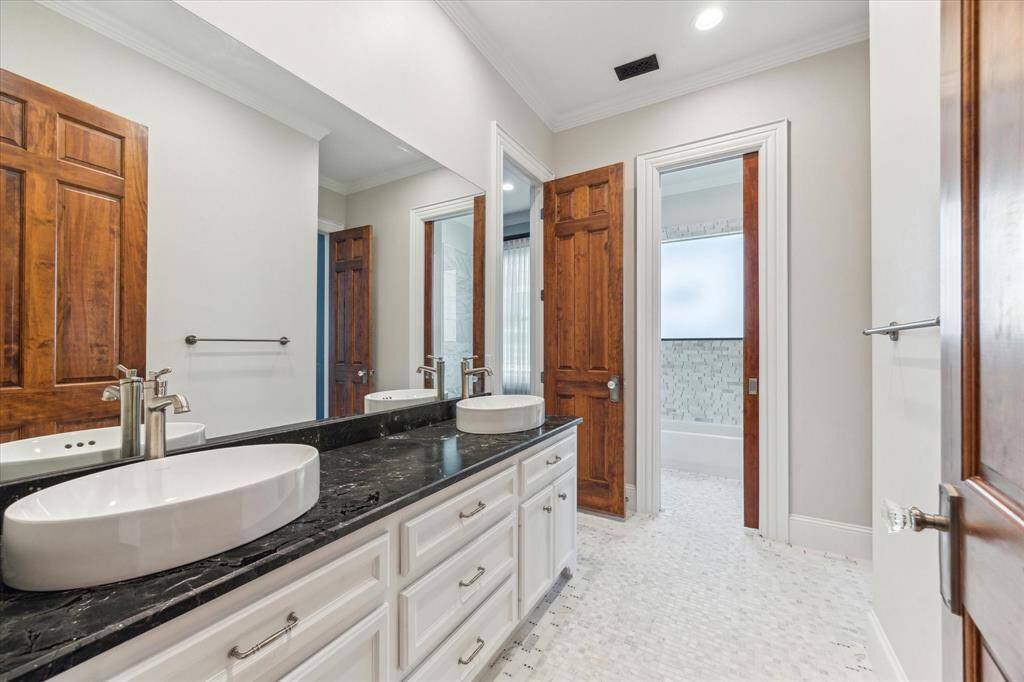 Elegant Secondary Bathroom: This stylish secondary bathroom features a sleek black granite countertop, a modern vessel sink, and crisp white cabinetry. Rich wood accents and a spacious layout create a perfect blend of luxury and functionality.