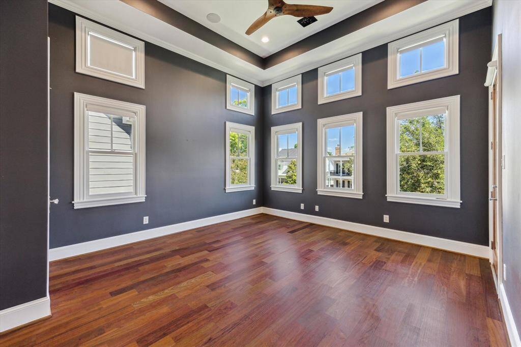 Stunning Third Bedroom: This sophisticated third bedroom features dramatic dark accent walls, a stylish tray ceiling with recessed lighting, and an abundance of natural light through multiple windows. Rich hardwood floors and a sleek ceiling fan complete this striking space.