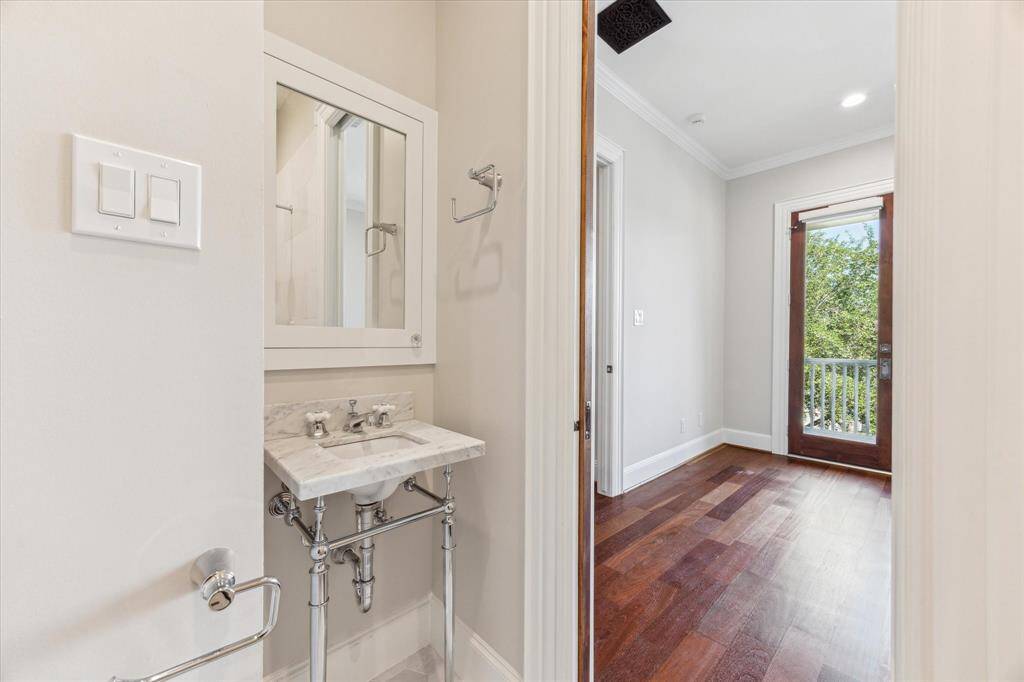 Chic En-Suite Bath: This private en-suite bathroom boasts a stylish pedestal sink with exposed chrome plumbing, a sleek glass shower, and direct access to a sunlit bedroom. A perfect blend of classic charm and modern functionality.