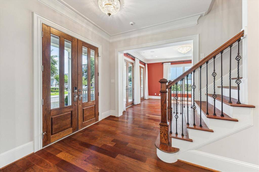 Grand Entrance with Timeless Elegance: Step inside to a light-filled foyer featuring rich hardwood floors, intricate wrought-iron staircase details, and expansive glass-paneled double doors. This sophisticated entryway sets the stage for an exceptional Houston Heights living experience.