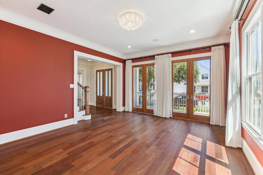 Sunlit Sophistication: Bathed in natural light from expansive French doors, this elegant space boasts rich hardwood floors and a striking deep-red accent wall, creating a perfect blend of warmth and grandeur. A versatile area for refined entertaining or peaceful everyday living.