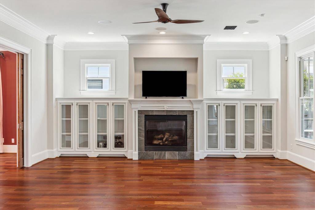 Sophisticated Fireside Elegance: Anchored by a grand fireplace framed in marble, this living area is enhanced by custom built-in cabinets with glass doors, offering both style and storage. The high ceilings and sleek ceiling fan add a touch of modern comfort to this refined space.