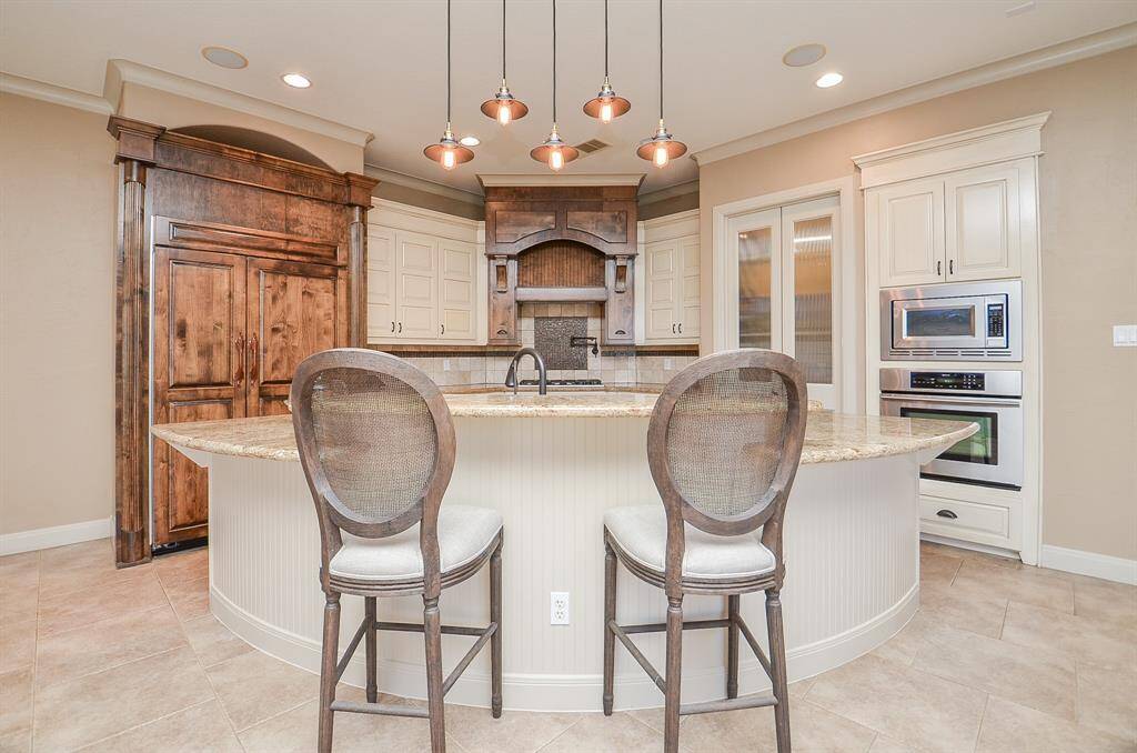 This kitchen features a captivating curved island that encompasses the sink and offers a delightful view of both the living area and the adjacent outdoor pool space. The curvature of the island adds an inviting touch to entertainment, allowing you to enjoy TV or observe pool and lake activities while preparing meals. Positioned to the right, concealed behind double doors, you'll find the butler's pantry and a spacious storage pantry.