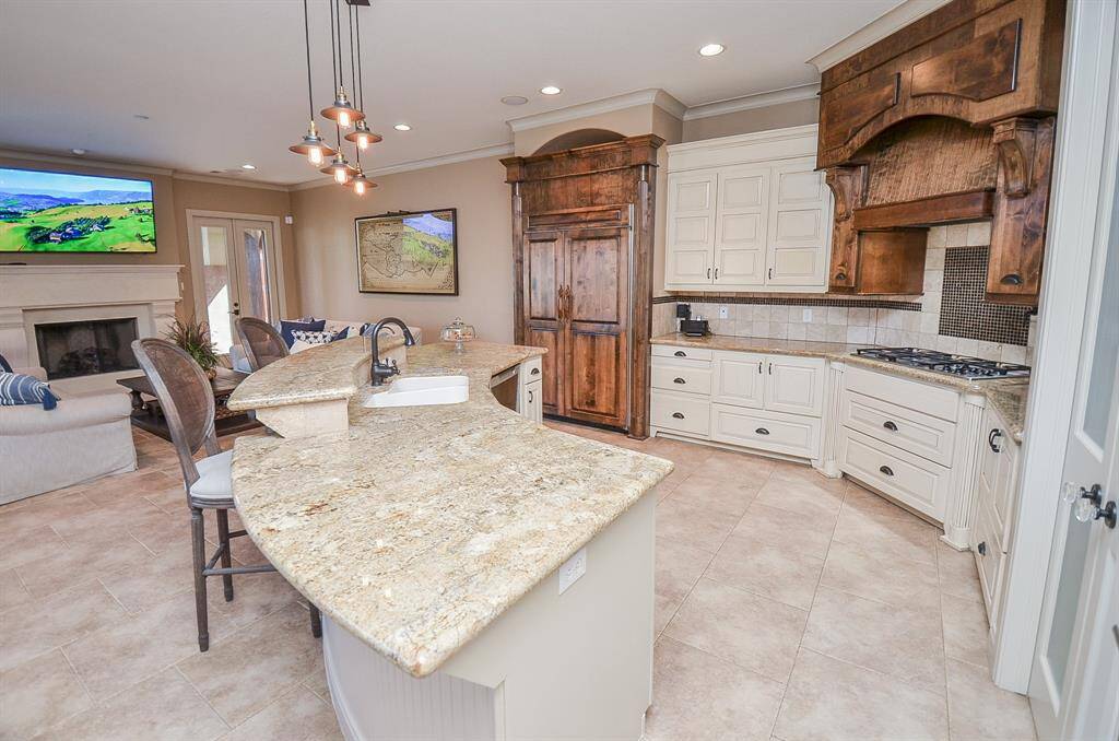 This open-concept living space seamlessly merges the kitchen and living room areas. It features a spacious layout where the kitchen area flows gracefully into the adjoining living room.  To the left not pictured is the breakfast area.  To the right (not pictured) is a butler's pantry and pantry.  Pot filler is above the stove.  Sink has a Reverse Osmosis system.  The refrigerator is integrated into the wooden cabinetry.