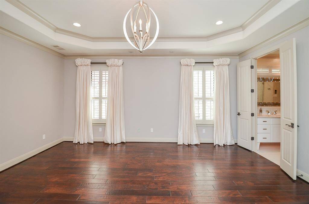 The primary bedroom boasts a cove ceiling, wooden flooring, and an exquisite design. For those inclined, you can even enjoy a peek at the lake from this room.  To the right you enter the primary bathroom.  Just beyond these doors lies a sitting room and an additional bar area equipped with a sink, refrigerator, and ice maker.