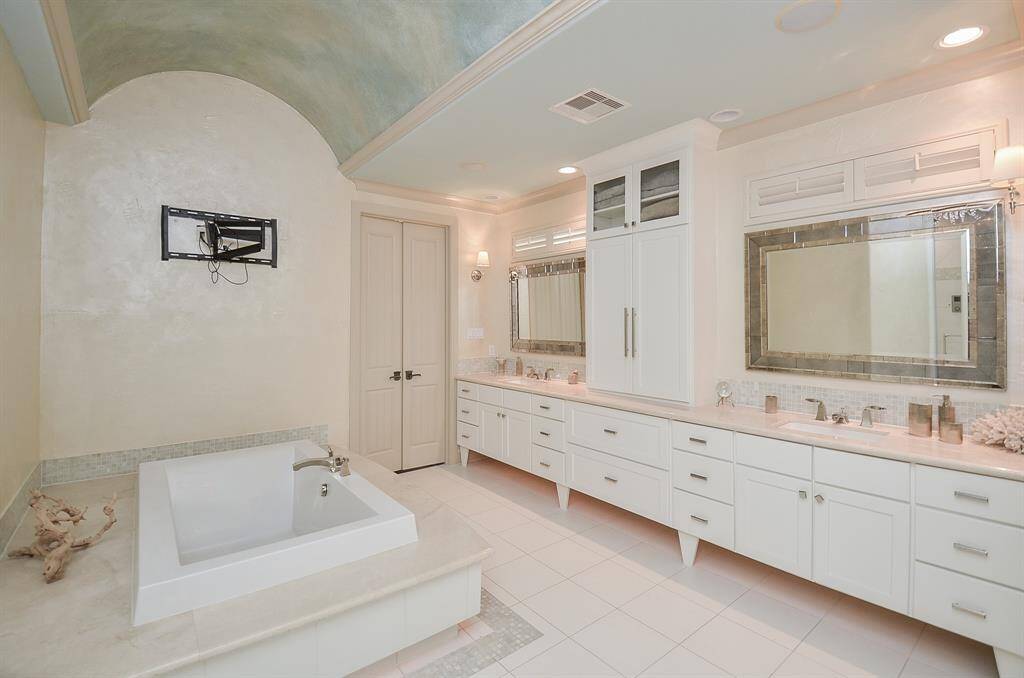The primary bathroom from a different perspective,  a close look at the gracefully arched ceiling, the ambient foot lighting, and the abundant natural light filtering in from above the mirrors. Every element has been meticulously attended to, with no corners cut. To the left (not pictured), there is a Kohler Steam Shower.  The bathroom has been prewired for TV.  Behind the double doors is the primary bedroom just pictured.