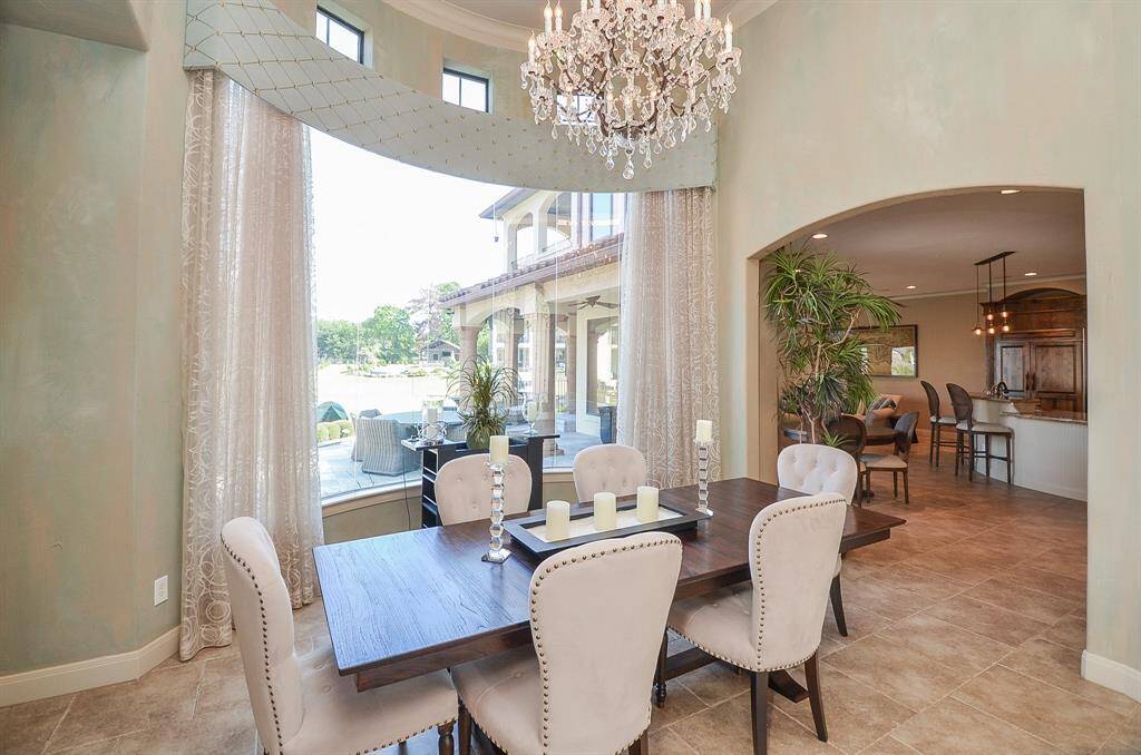 The formal dining area features a captivating curved glass wall that provides picturesque views of the pool. To the left (not pictured) the double doors lead to guest rooms and the first-floor suite.